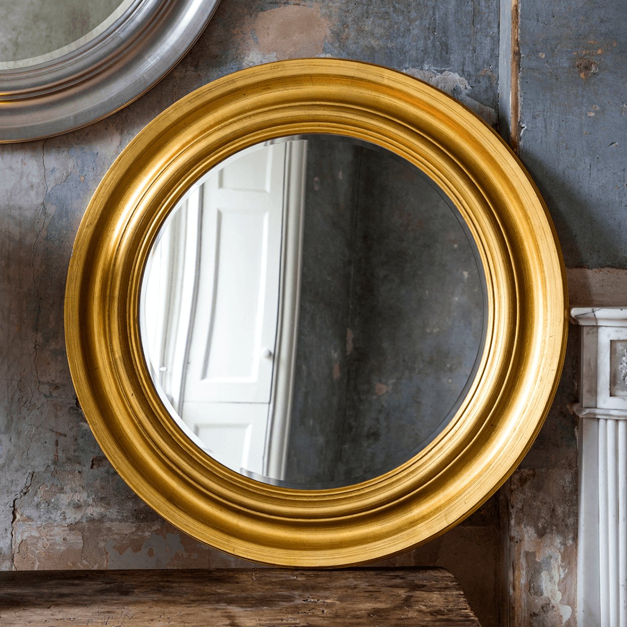 round gold mirror in front of aging wall